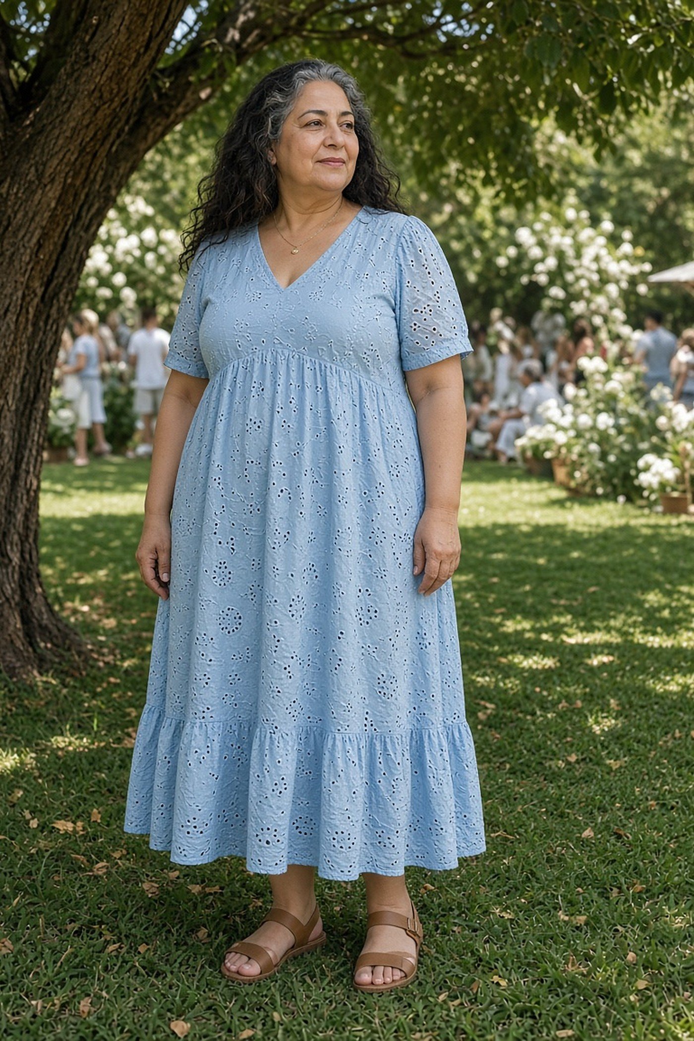 Woman over 50 in a powder-blue eyelet cotton midi dress under a tree