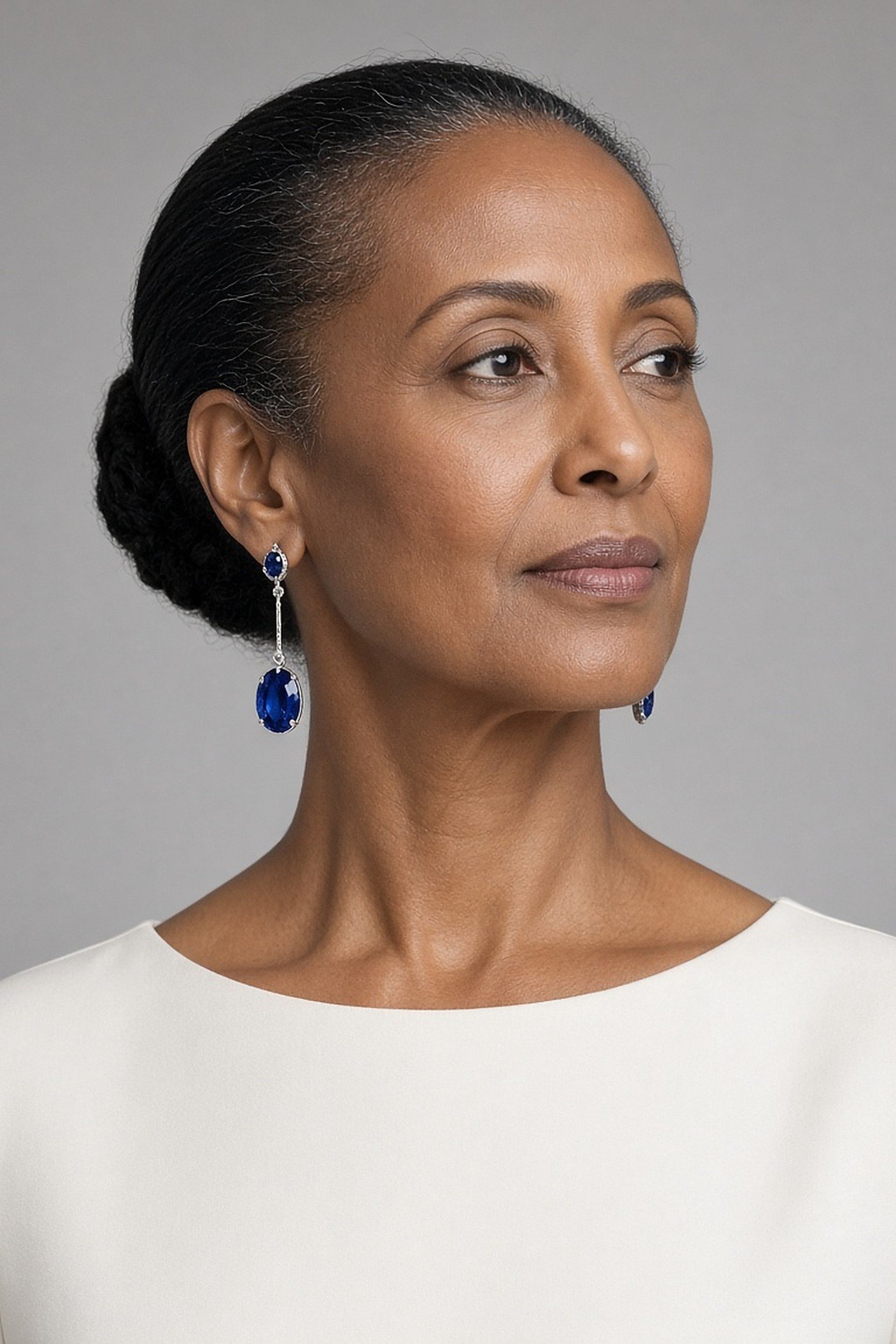 Woman over 50 wearing sapphire drop earrings with an off-white top