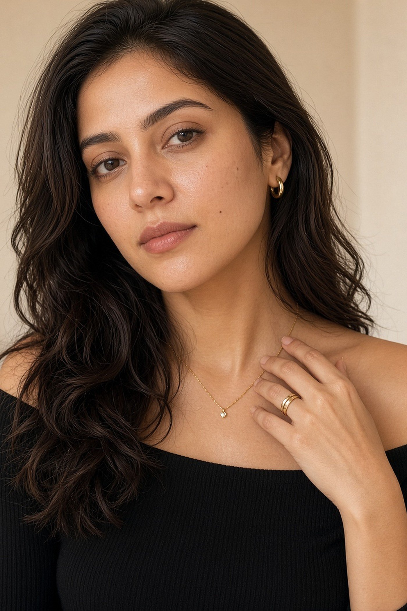 Woman in her 30s wearing a fine gold necklace, hoops and stacking ring
