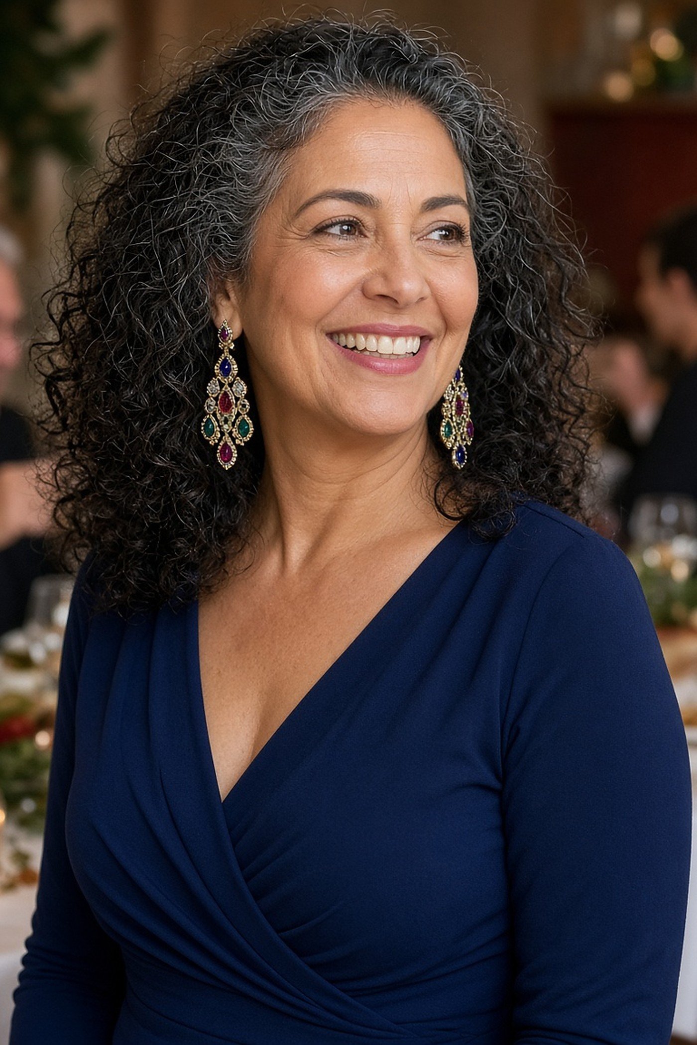 Woman over 50 wearing jewel-tone dangle earrings with a navy wrap dress
